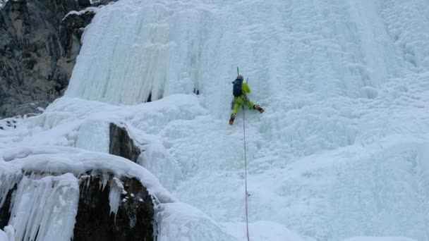 Альпинист с топором для льда взбирается на замерзший водопад, большую стену со льдом — стоковое видео