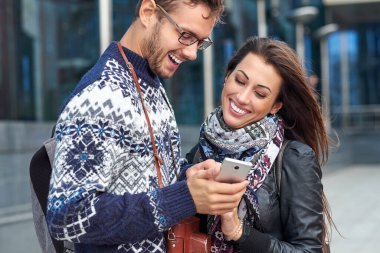 Akıllı telefonu olan mutlu bir çift. Dışarıda birlikte durup cep telefonuna bakan mutlu genç çift.