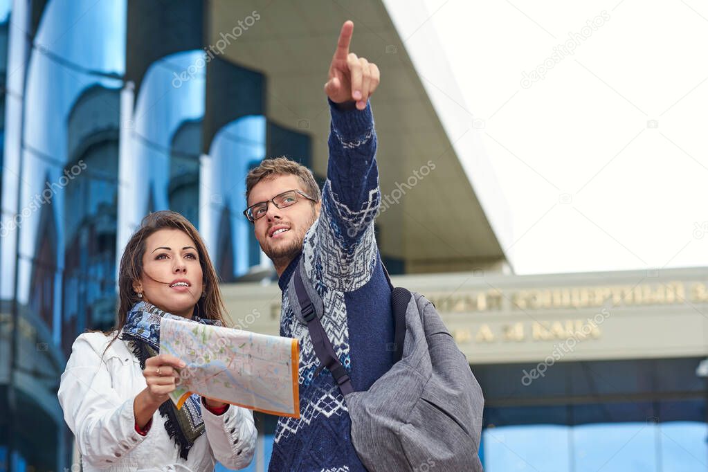 two happy tourists couple searching location together with a phone and map and pointing with the finger.