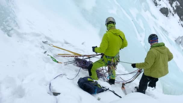 Два альпиниста на страховке готовятся подняться на замерзший водопад — стоковое видео