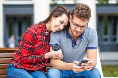 Akıllı telefonu olan mutlu bir çift. Dışarıda birlikte durup cep telefonuna bakan mutlu genç çift.
