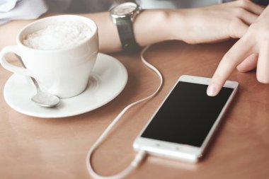 Akıllı telefonları, kulaklıkları ve bir fincan çayı olan kadın elleri. Grafik görüntüleme montajı için