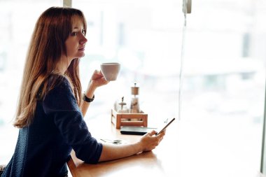 Akıllı telefonunu kullanarak ve kahve dükkanında gülümseyen genç iş kadını.
