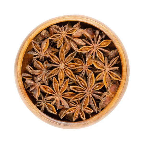 Star anise fruits and seeds, in a wooden bowl. Also known as staranise, star aniseed or badian. Dried, star-shaped pericarps of Illicium verum, containing anethole, a spice with intense anise flavor.