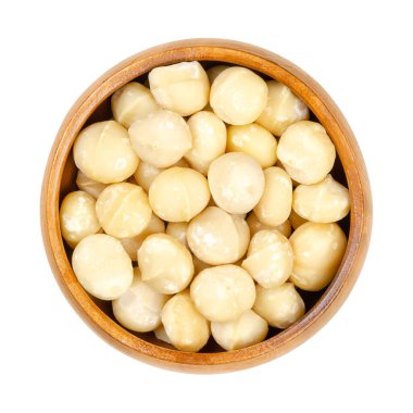 Kabuklu ve kurutulmuş macadamia fındıkları, ahşap bir kasede. Ayrıca Queensland, Bush, Maroochi, Bauple veya Hawaii fıstığı olarak da bilinir. Güzel atıştırmalık. Yakın plan, yukarıdan, beyaz arkaplanda izole edilmiş, makro yiyecek fotoğrafı.