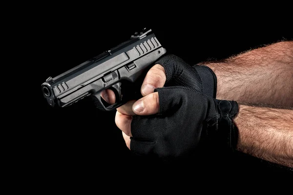 Closeup man hand with gloves holding gun with two hands and aiming down on black background. Finger on the trigger of the pistol.
