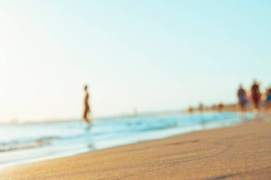 Yaz tatilinde gün doğumunda deniz kıyısındaki insanların bulanık siluetleri. Ön plana odaklan. Sığ alan derinliği. 