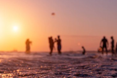 Silhouettes of blurry people on the seashore during sunset in summer in Antalya. Focus on foreground. Ripples and reflections on water surface. Tropical summer holiday.