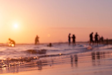 Silhouettes of blurry people on the seashore during sunset in summer in Antalya. Focus on foreground. Ripples and reflections on water surface. Tropical summer holiday. 