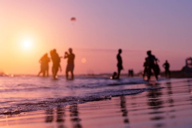 Silhouettes of blurry people on the seashore during sunset in summer in Antalya. Focus on foreground. Ripples and reflections on water surface. Tropical summer holiday. 
