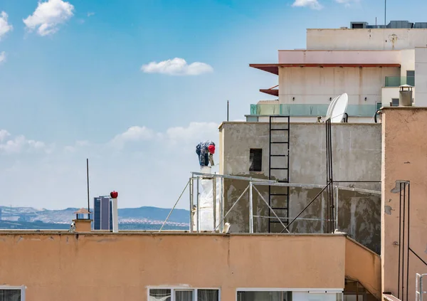 Profesyonel inşaat işçisi çatıdaki yüksek bina cephesini tamir ediyor. Bulutlu mavi gökyüzünün önündeki binanın dış duvarını alçılayan ön cephe ressamı.