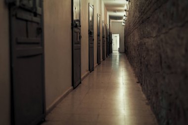 Karanlık klostrofobik koridor ve bir hapishanede kilitli hücre kapıları. Özgürlükten mahrum olmak. Koridorun sonunda açık bir kapı var.. 