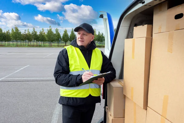 Unloading boxes in cargo van. The postman checks the shipping address. Delivery of parcels. A man performs an order for the carriage of the boxes. Mailman at work. Logistics Concept.