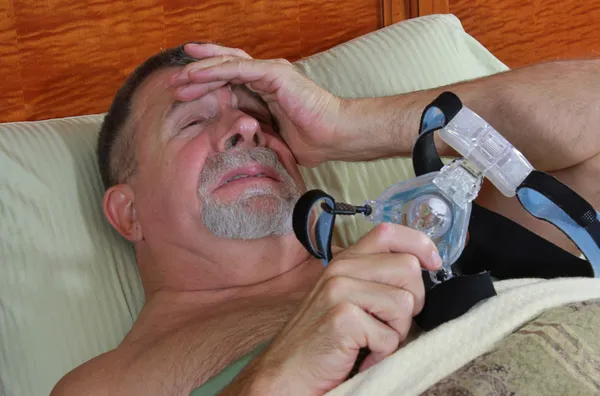 Senior adulto uomo frustrato con il suo CPAP a letto Fotografia Stock