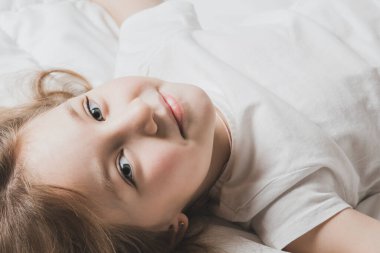 Güzel küçük kız beyaz çarşaflarla yatakta yatıyor. Ev konforunun sıcaklığı