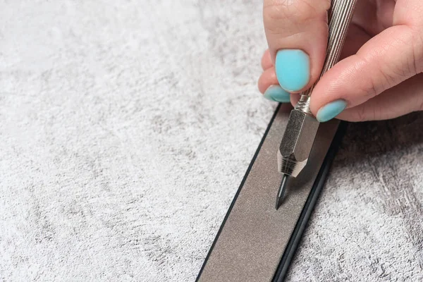 Womans hand with manicure sharpens scraper on diamond bar. Mechanical cleaning of coins and archaeological items