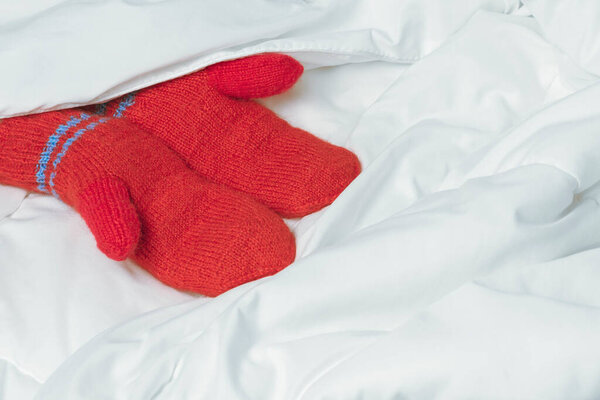 Womens hands in red mittens on white blanket. The warmth of home comfort