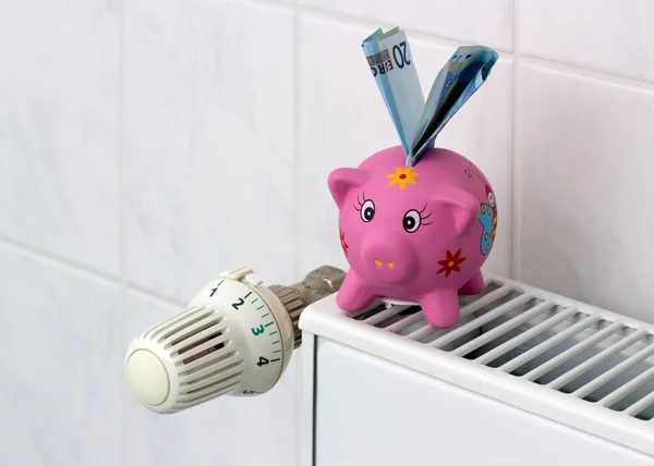 Piggy bank with radiator thermostat saving heating costs Royalty Free Stock Images