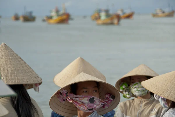 Vietnamese women in traditional conical hats "non" wait fishing boats on the beach in Mui Ne, Vietnam. — Stock Photo, Image