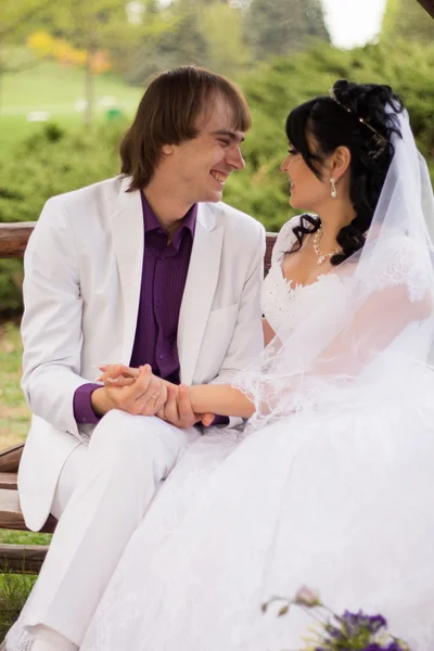 Casal apaixonado noiva e noivo posando sentado no banco de madeira em — Fotografia de Stock