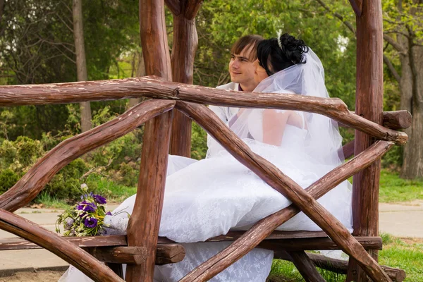 Casal apaixonado noiva e noivo posando sentado no banco de madeira em — Fotografia de Stock