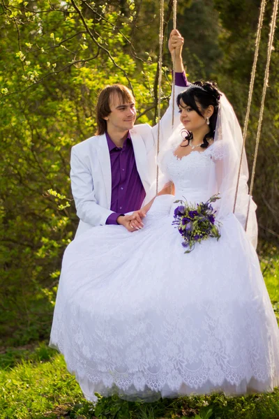Bruid en bruidegom swingen op een schommel — Stockfoto