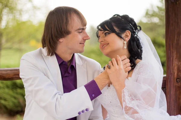 Casal apaixonado noiva e noivo posando sentado no banco de madeira em — Fotografia de Stock