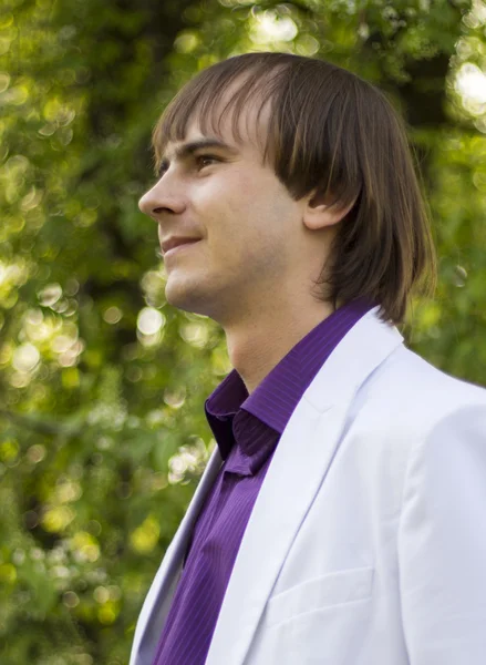 Счастливый парень в парке в белом костюме и фиолетовой рубашке — стоковое фото