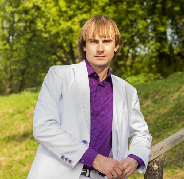 Serious guy in the park a white suit and purple shirt — Stock Photo, Image