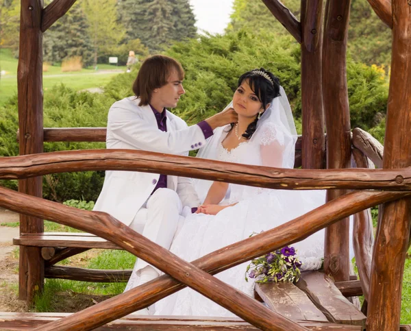 Coppia innamorata sposa e sposo in posa seduta su panca di legno in — Foto Stock