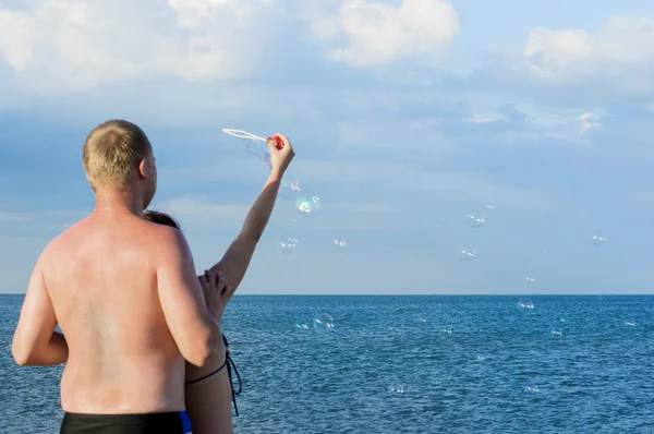 The guy and the girl start soap bubbles on the sea. The view fro — Stock Photo, Image
