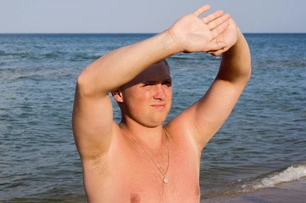 Buen tipo entrecerrando los ojos al sol en la playa — Foto de Stock