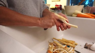 Bir kadın mutfağında havuç ve yaban havucu soyar.