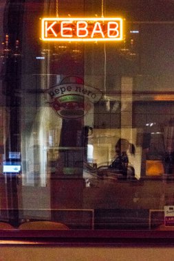 Stockholm, İsveç. Geceleri bir restoranın önünde kebap tabelası ve silüet giymiş bir insanın yansıması..