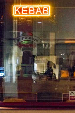 Stockholm, İsveç. Geceleri bir restoranın önünde kebap tabelası ve silüet giymiş bir insanın yansıması..