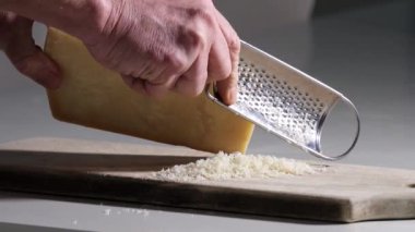Parmesan peynirini ahşap kesim tahtasında rendeliyor.