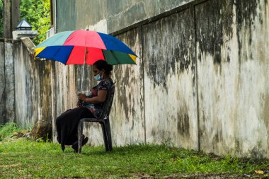 Galle, Sri Lanka Bir kadın sıcaktan korunmak için renkli bir şemsiye altında oturuyor.