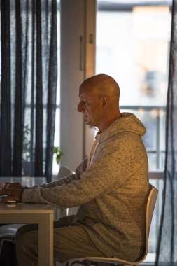 Stockholm, İsveç 'te bir adam sabahın erken saatlerinde mutfakta oturur ve bilgisayarla çalışır..