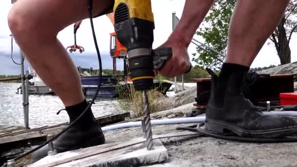 スウェーデンのストックホルム湖の上にドックを構築しながら 男は岩にドリルパワードリルを使用しています — ストック動画