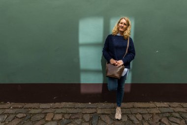 Riga, Letonya, bir kadın turist güneşte yeşil bir duvara yaslanıyor..
