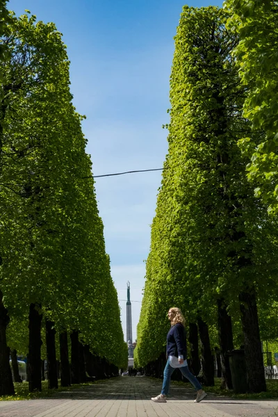 Riga Lotyšsko Žena Kráčí Uličce Lemované Stromy Centru Města Památníkem — Stock fotografie