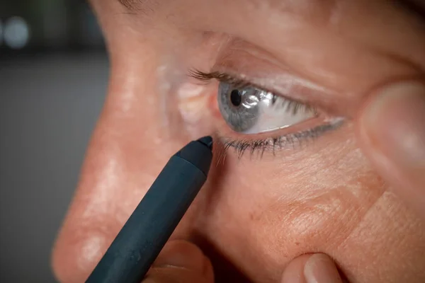 A woman applies an eye liner to her eyes.