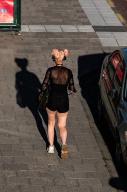 Stockholm, İsveç. Kulaklıklı genç bir kadın. Güneşte Hantverkargatan boyunca yürüyor..