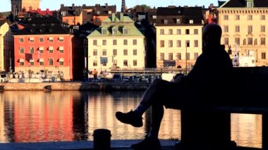 Stockholm, İsveç 'te bir adam Skeppsholmen' de su manzaralı bir bankta oturuyor ve Gamla Stan, ya da Old Town. 