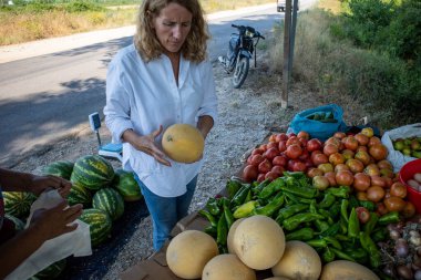 Arnavutluk 'un Ksamil kentinde bir kadın turist yol kenarındaki çiftlik tezgahından sebze alıyor.