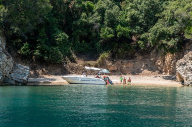 Arnavutluk 'un Ksamil kenti ve turistlerle ıssız bir plaja gezintiye çıkan küçük bir motorlu tekne.
