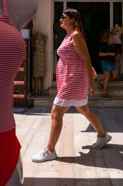 Arnavutluk 'un Permet kentinde çizgili bluz giyen bir kadın çizgili bluzla dükkanın önünden geçiyor..