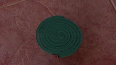 A burning anti-mosquito coil on a stand outdoors and smoke