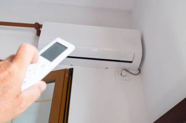 Bir adam klimayı ayarlamak için uzaktan kumanda kullanıyor..