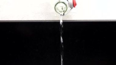 A glass water bottle is emptied into a sink in a kitchen